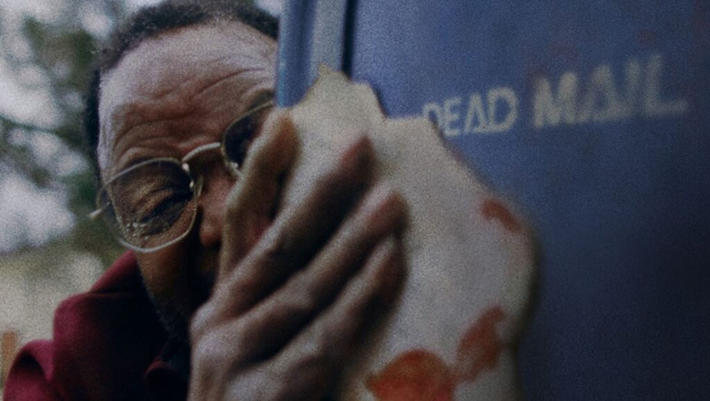 Pepe film review: Man with glasses holds Dead Mail box. Nelson Carlos de los Santos Arias film still.