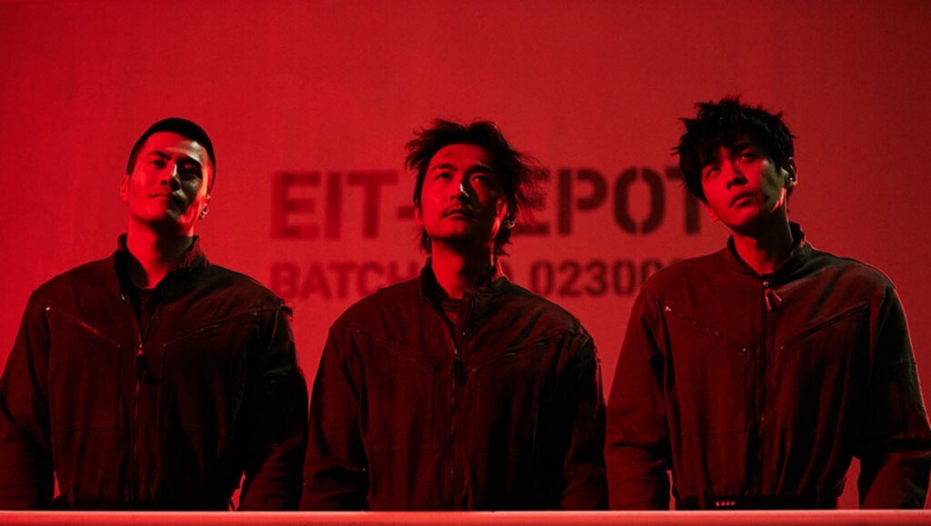 Seeds movie still: Three actors in jumpsuits stand against a red backdrop. TIFF '24 film review.