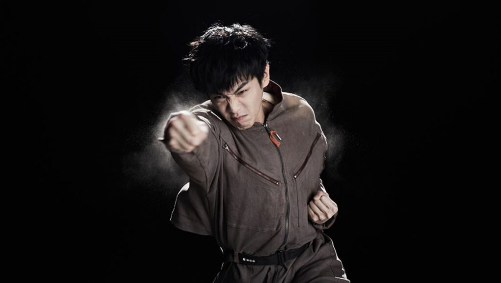 Still from Seeds (TIFF '24 Review): Kaniehtiio Horn. Man in jumpsuit throws a punch against a black background.