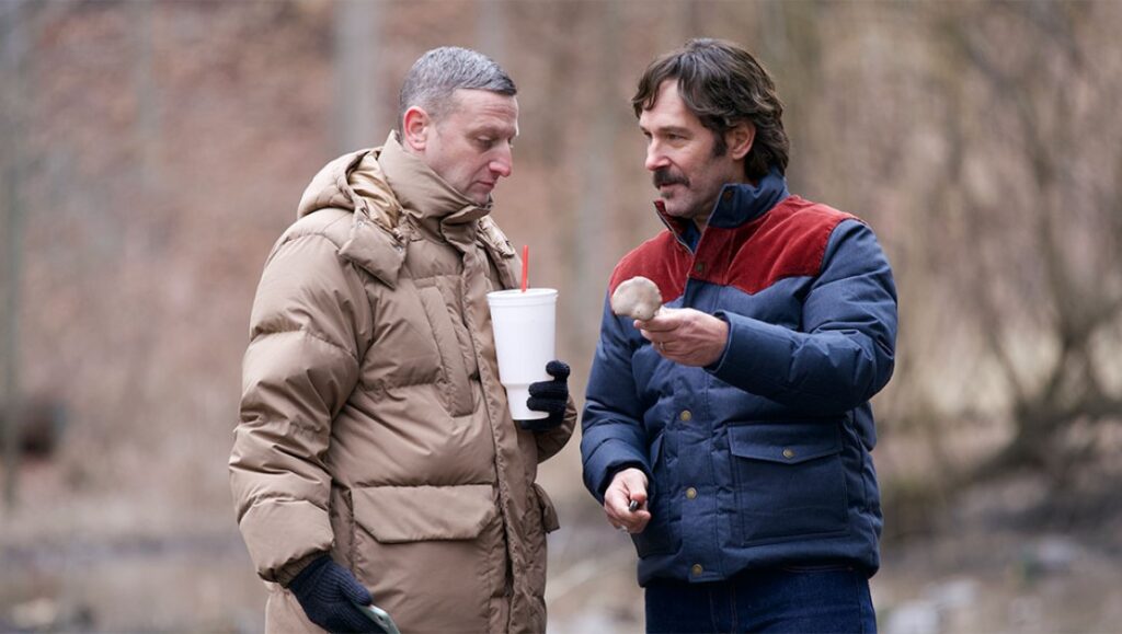 Two friends in winter jackets. One holds a drink, the other a mushroom. Friendship and outdoor scene.