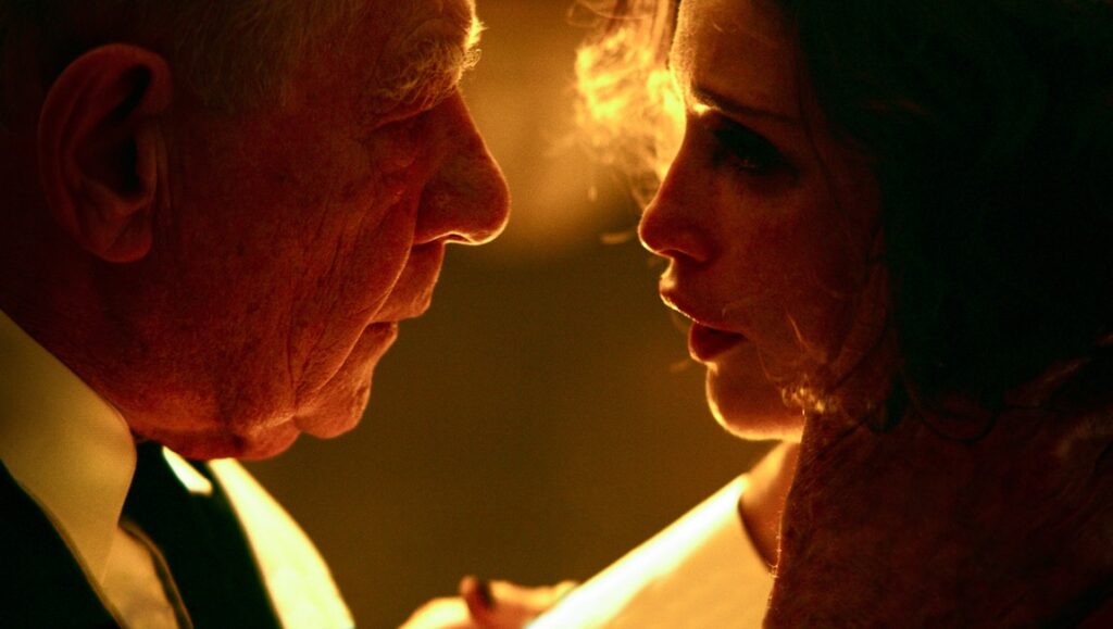 Ian McKellen and Gemma Arterton in The Critic movie. Close up of the actors facing each other.