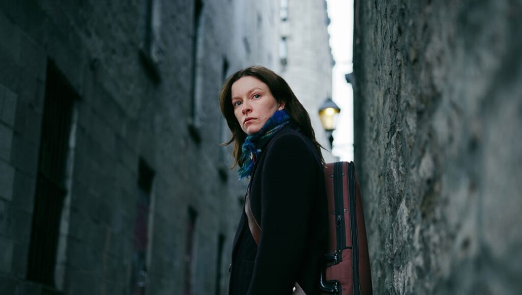 Measures for a Funeral film still: Woman with suitcase in alley. TIFF '24 review.