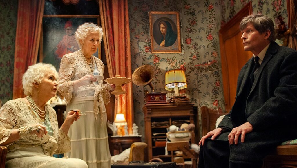 Still from Measures for a Funeral at TIFF '24. Three people in a floral wallpapered room with vintage decor.