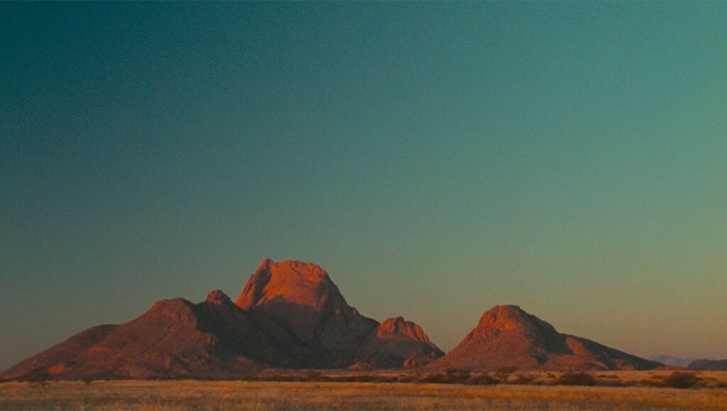 Landscape from Pepe film review. Mountains under a teal sky. Arid, golden landscape.