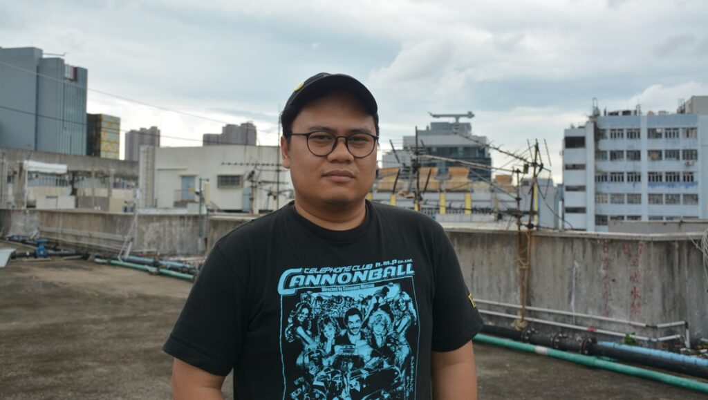 Riar Rizaldi, Indonesian filmmaker. Portrait of Riar Rizaldi, wearing a Cannonball Run t-shirt, with city buildings in the background.