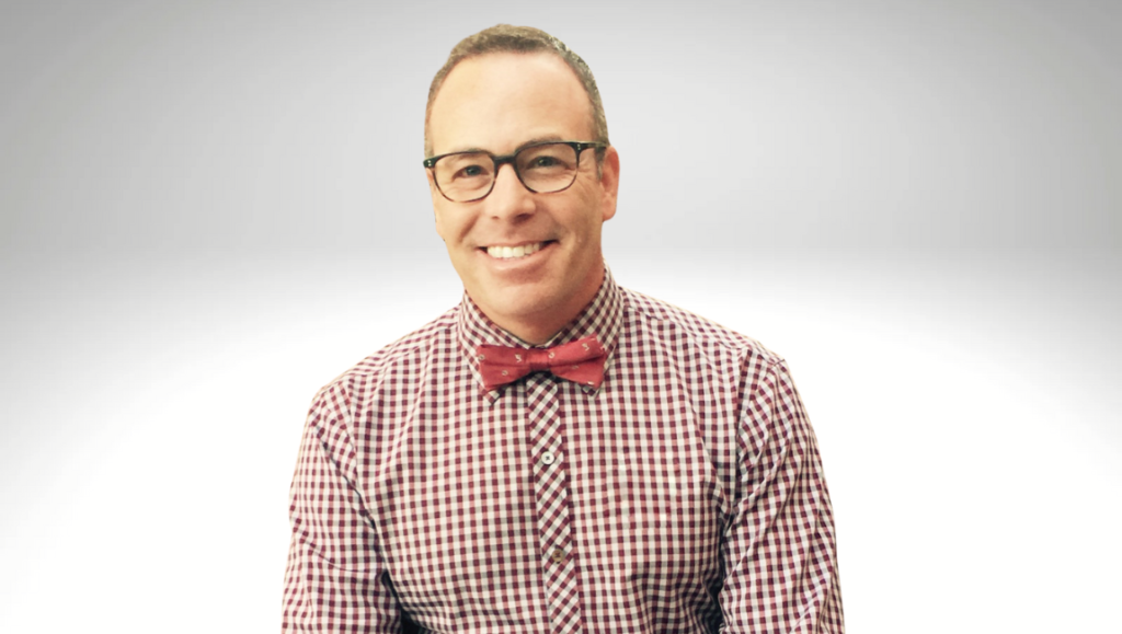 Stephen Soucy portrait. Man with glasses, bow tie, and checkered shirt smiling. Interview with Stephen Soucy.