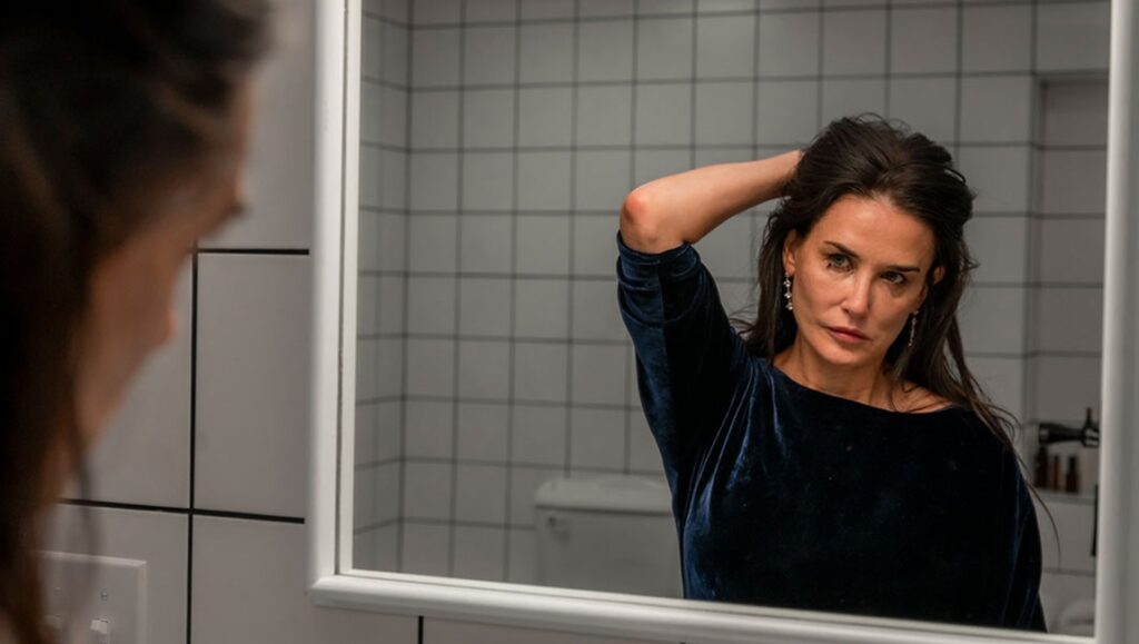 The Substance movie still. Demi Moore looks in a mirror with smeared makeup. TIFF '24 review.