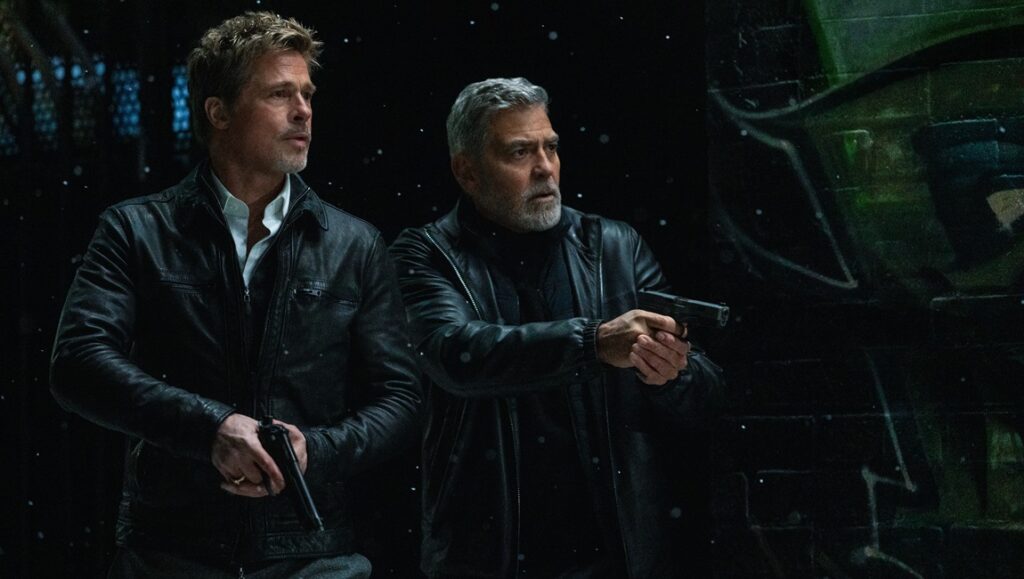 The Wolves movie still: Brad Pitt and George Clooney hold guns in a dark, gritty scene.