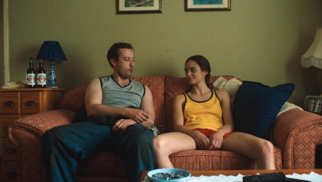Hoard film review: Man and woman sit on a couch in a still from Luna Carmoon's Hoard.