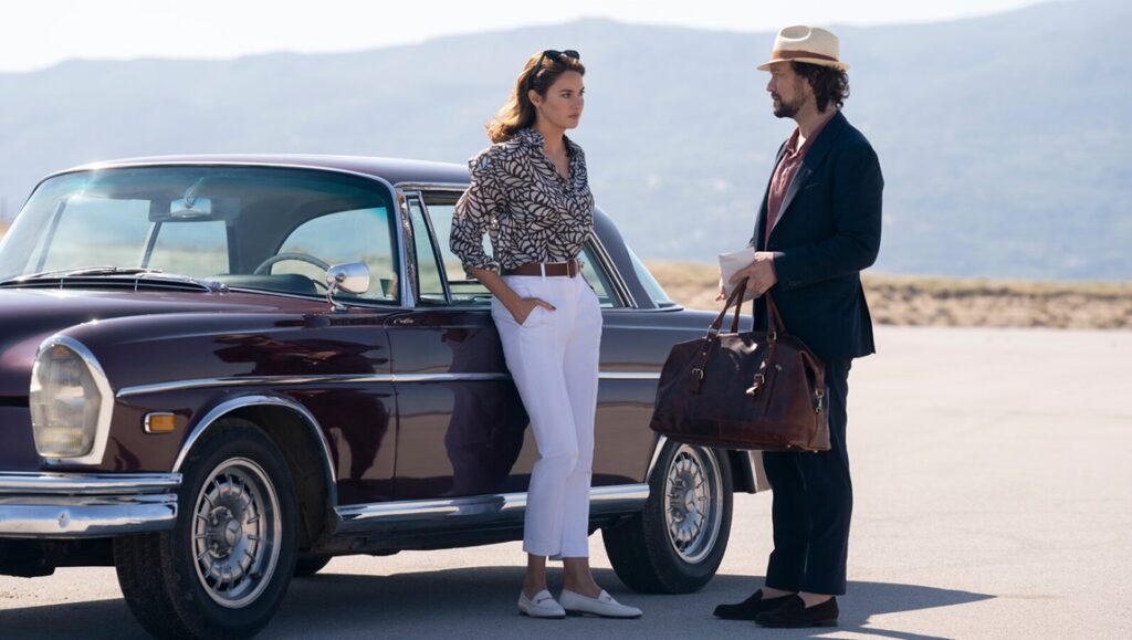 Adam Driver and Nathalie Emmanuel in Francis Ford Coppola's Megalopolis, standing by a vintage car.