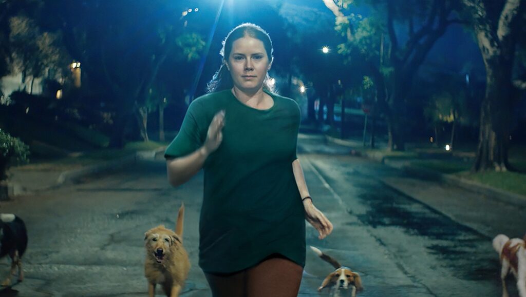 Amy Adams in Nightbitch movie still. Woman jogging with dogs at night. TIFF '24 review.