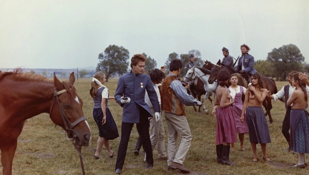 Scene from Miklós Jancsó's Red Psalm film. Features horses, soldiers, and peasants in a field.