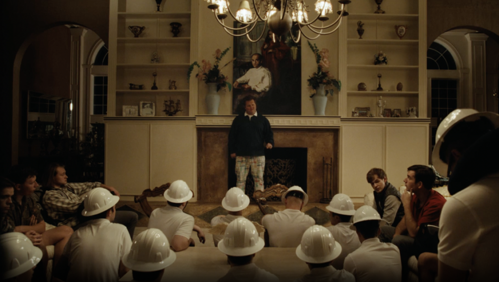 The Line movie scene. Man addresses students in hard hats in a grand room with fireplace.