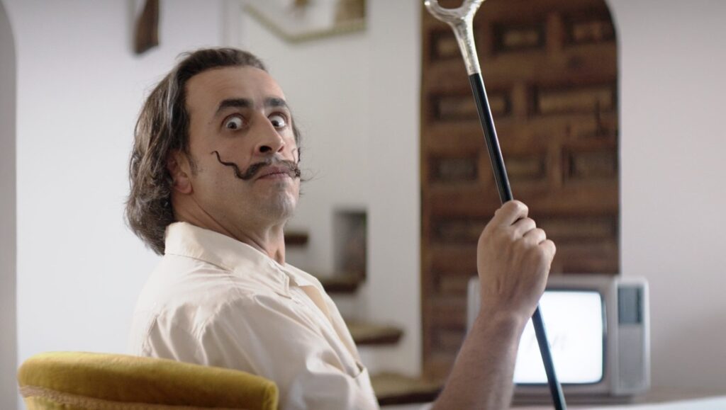 Still from Daaaaaalí!: Salvador Dalí (actor) with cane, mustache, and wide eyes. Quentin Dupieux film review.