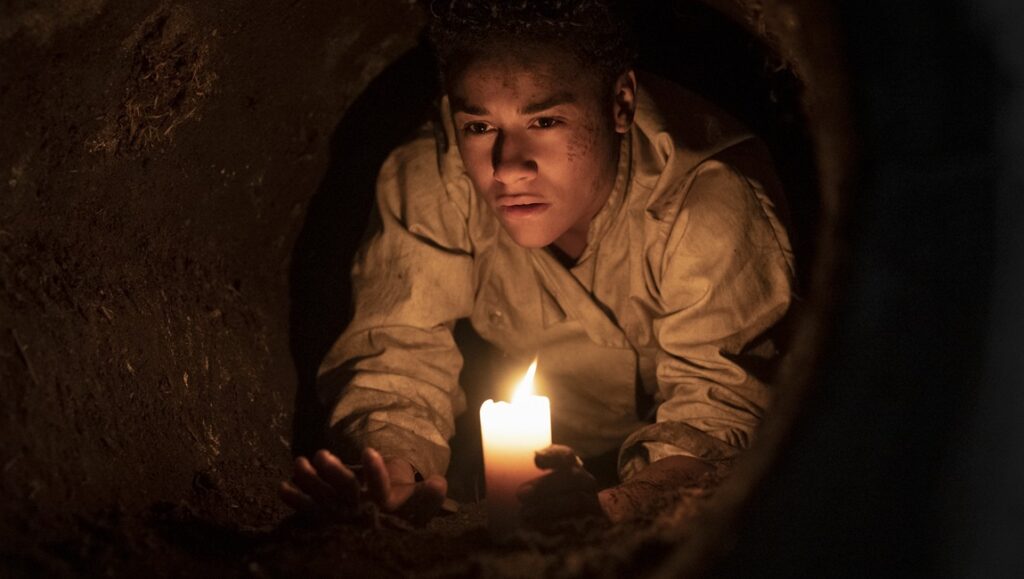 House of Spoils movie scene: Young actor with candle in dark tunnel. Horror film review.