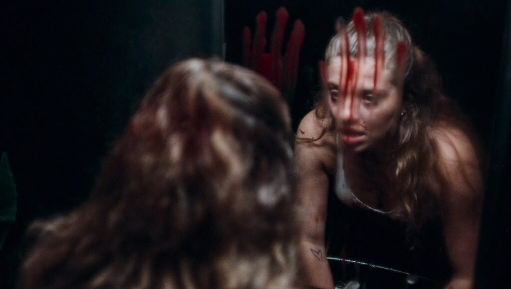 MadS movie still: Woman with blood on face and handprint on mirror. Horror film scene.