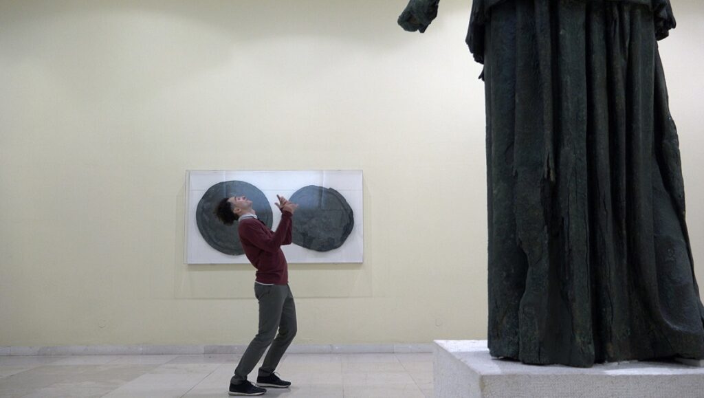 A Traveler's Needs film still. Man reacting to statue in art gallery. Hong Sang-soo movie review.