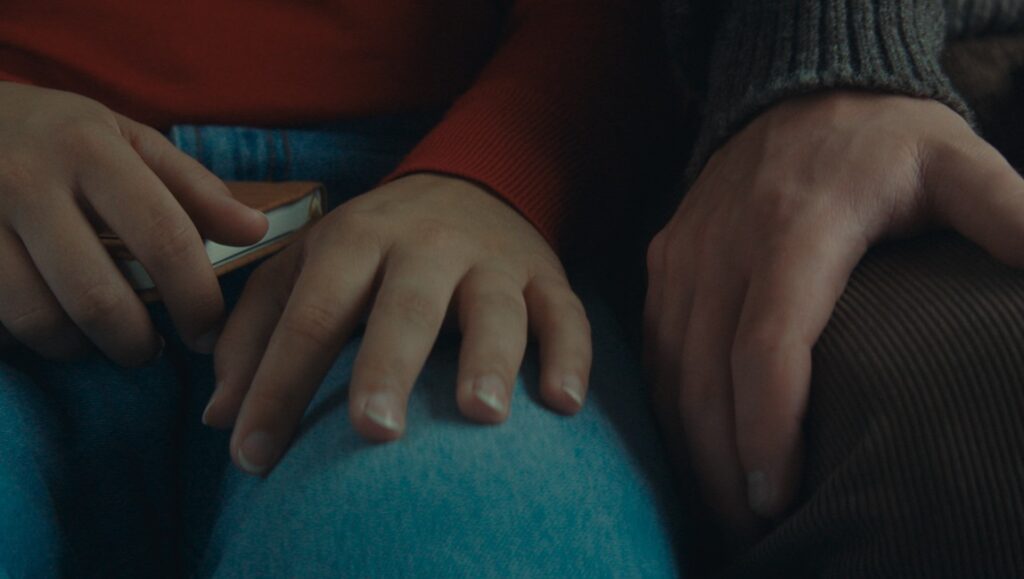 Who By Fire still: Hands holding a book. Philippe Lesage film review. NYFF62.