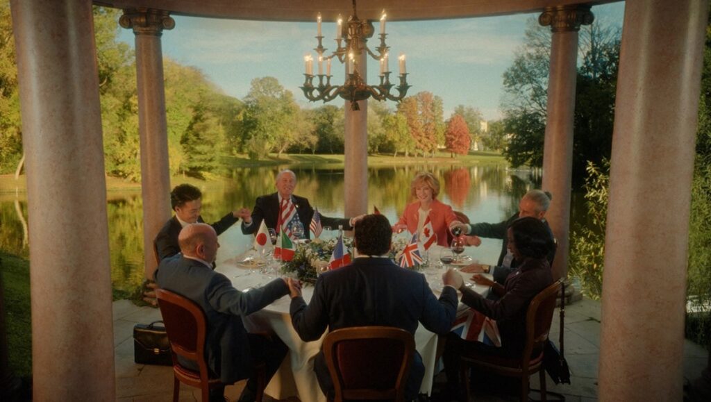 Still from Rumours, directed by Guy Maddin. Political leaders at a round table holding hands with flags.