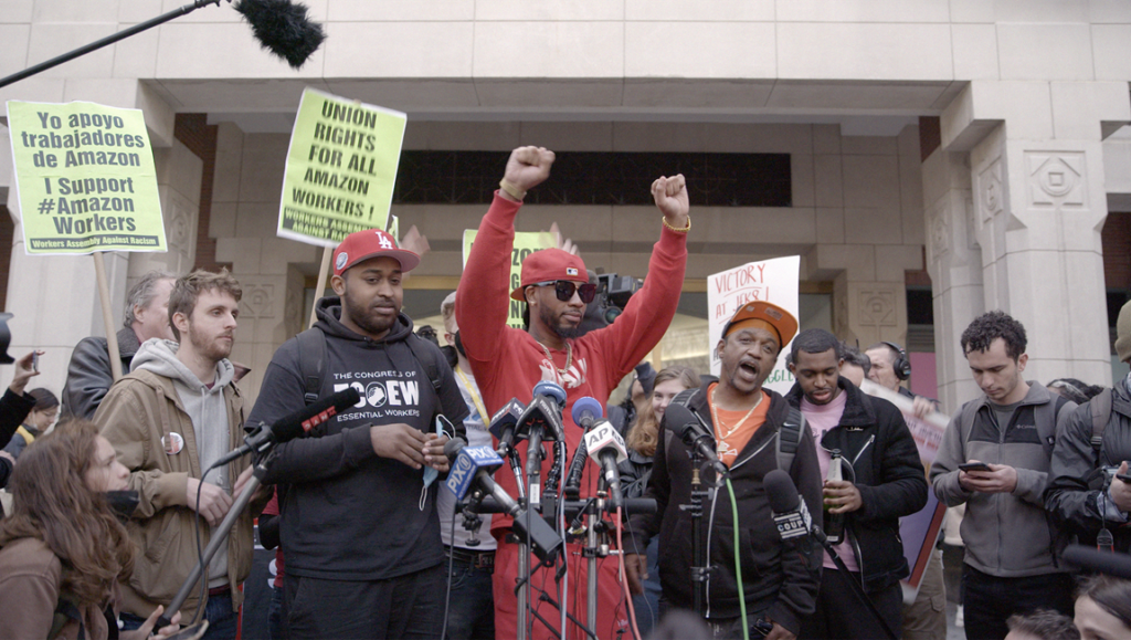 Still from Union documentary review. Amazon workers rally for union rights. Protestors with signs and raised fists.