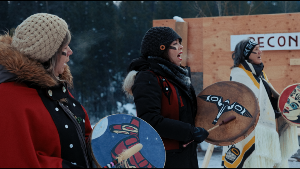 Yintah film: Indigenous women singing, drumming. Traditional First Nations regalia, face paint, winter scene.