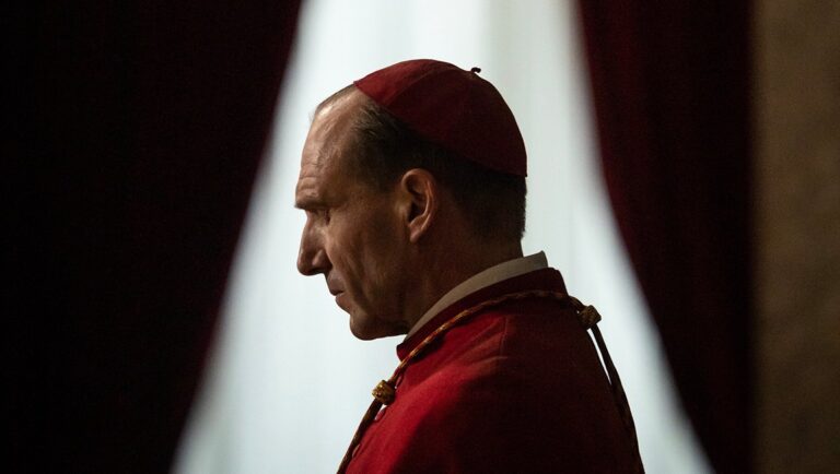 Ralph Fiennes as Cardinal in Conclave movie. Profile view of the actor wearing red cardinal robes.