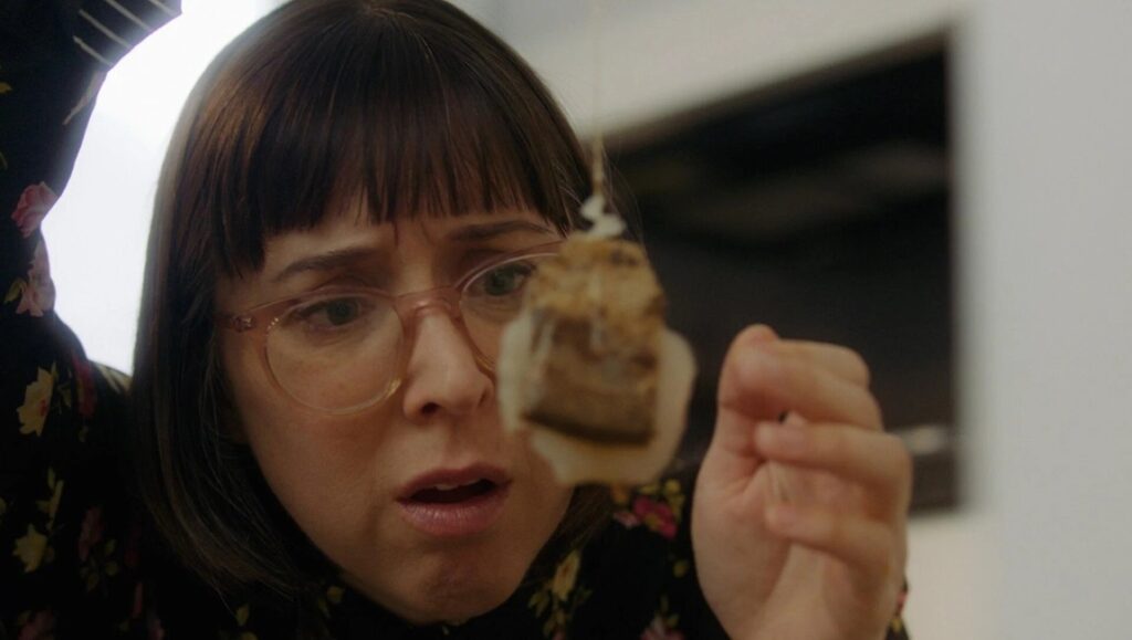 Darla in Space review: Woman with glasses examines a tea bag with a worried expression.