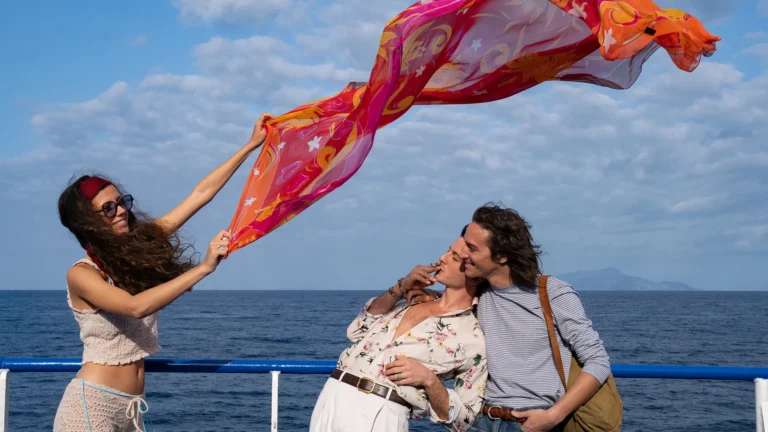 Parthenope film scene. Woman holds scarf over kissing couple on a boat with ocean backdrop. Paolo Sorrentino film review.