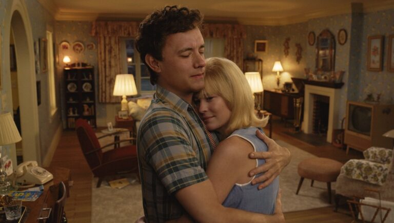 Here (2024): Robert Zemeckis film still. A man and woman embrace in a vintage-style living room. Movie review.