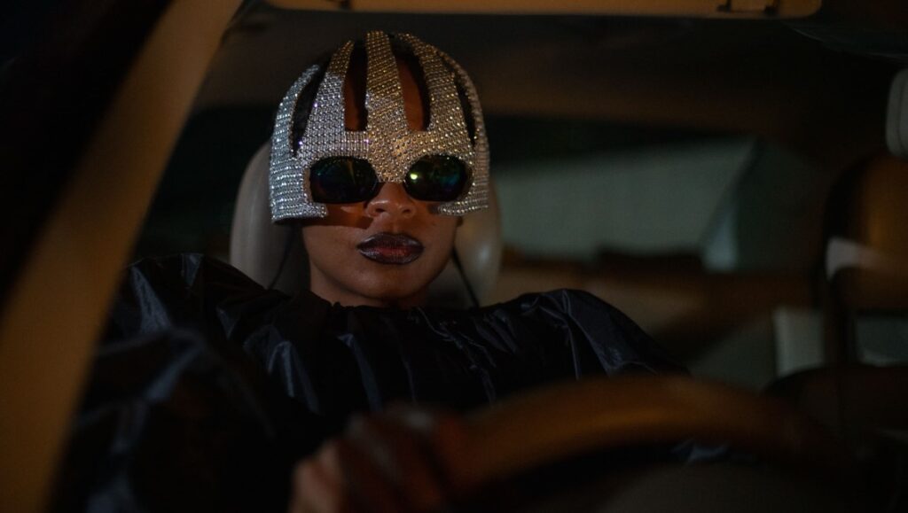 Woman driving in On Becoming a Guinea Fowl review. She wears a jeweled helmet and sunglasses.