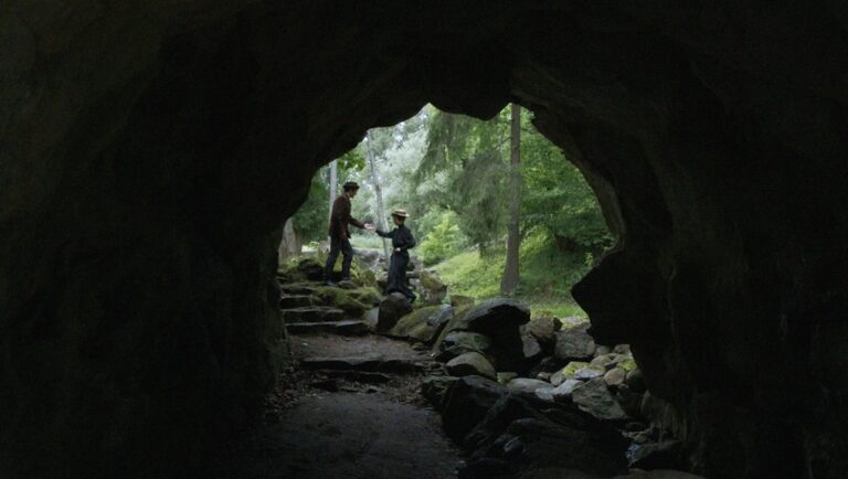 Deimantas Narkevičius' Twittering Soul review. Couple in period clothing stands outside a dark cave entrance.