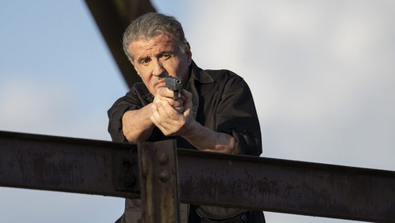Sylvester Stallone in Armor movie review. Actor aims a handgun. Action film.