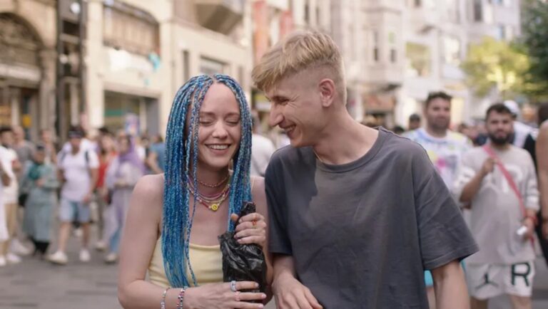 Deaf Lovers film review image: Smiling couple with blue braids on a crowded street. PÖFF '24.