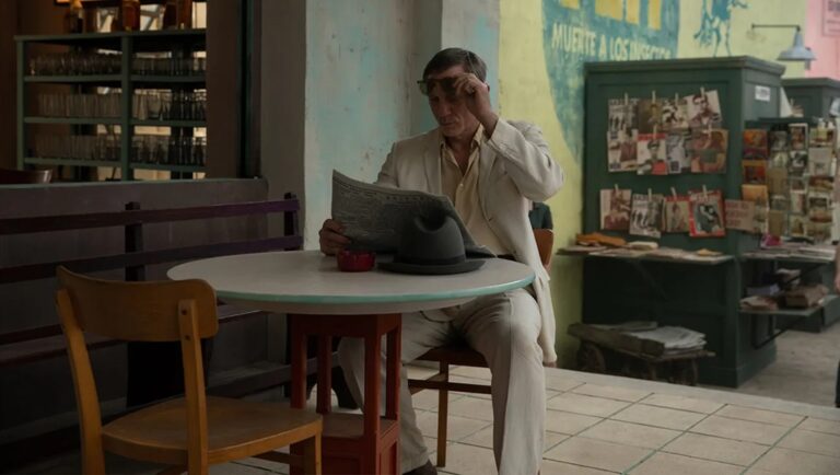 Still from Queer (2024) movie. Man reading newspaper at outdoor cafe. Luca Guadagnino film review.