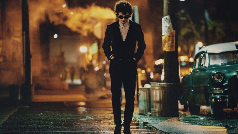 Jack Harlow as Bob Dylan in A Complete Unknown movie. Harlow walks on a wet street at night.
