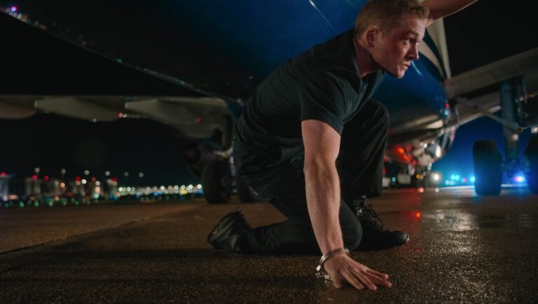 Carry-On movie scene. Man in handcuffs kneels by a plane at night. Action, thriller.