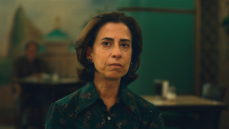 I'm Still Here film still: Woman in a patterned blouse with a serious expression. Movie scene.