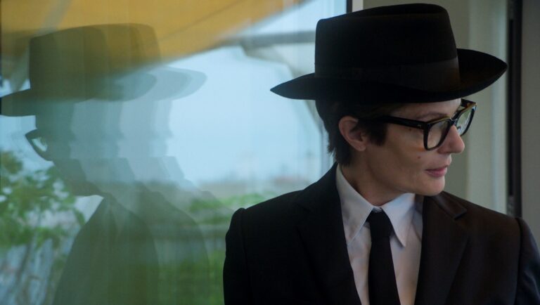 Man in hat and suit. Marcello Mio film still. Actor with glasses. Stylish, classic fashion. Reflection visible.