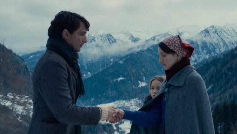 Vermiglio movie review: Man and woman shaking hands in a snowy mountain landscape.