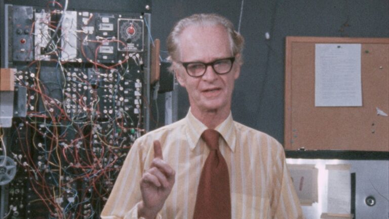 BF Skinner plays himself in Doc Fortnight film. Man with glasses, circuit board, and bulletin board.