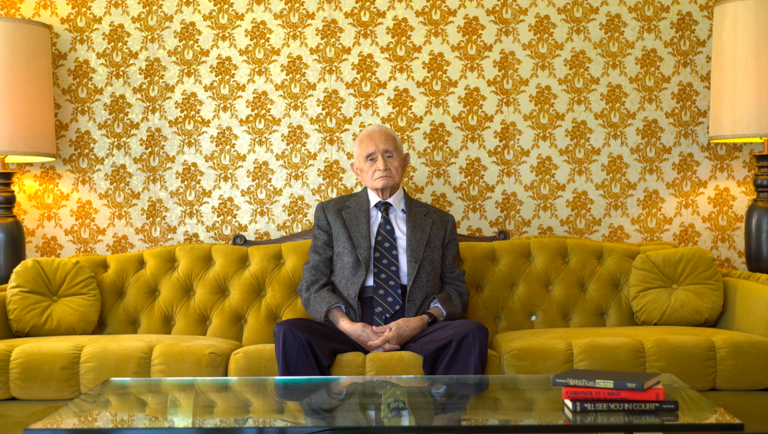 Billy Ray Brewton in Coroner to the Stars at Slamdance Film Festival. Man sits on yellow couch.