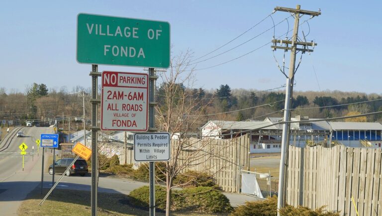 Village of Fonda sign. Road with street signs, No Parking and Attractions signs. Fonda, New York.