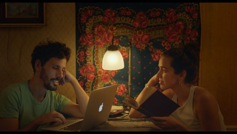 Still from The Klezmer Project film review. Man and woman at table with laptop and book.