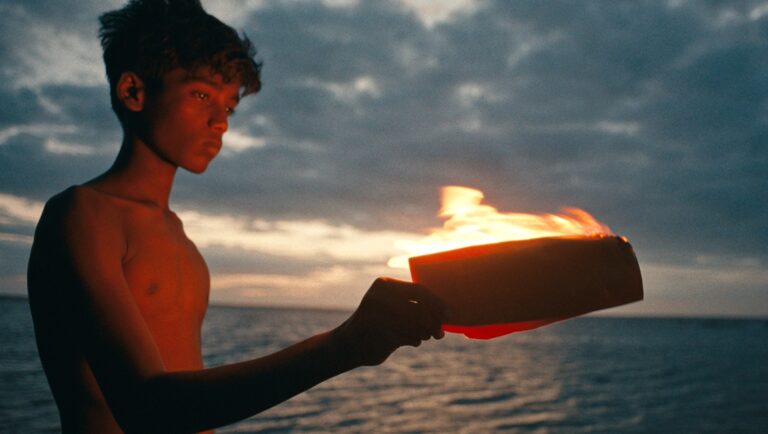 Young man holding fire at sunset. Ocean backdrop, dramatic sky. Ritualistic scene.