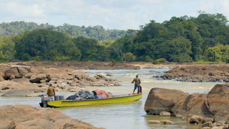 Film still from Cinéma du Réel 2025 film, *Little Boy, Paul, Evidence*. A yellow boat navigates a rocky river with lush forest backdrop.
