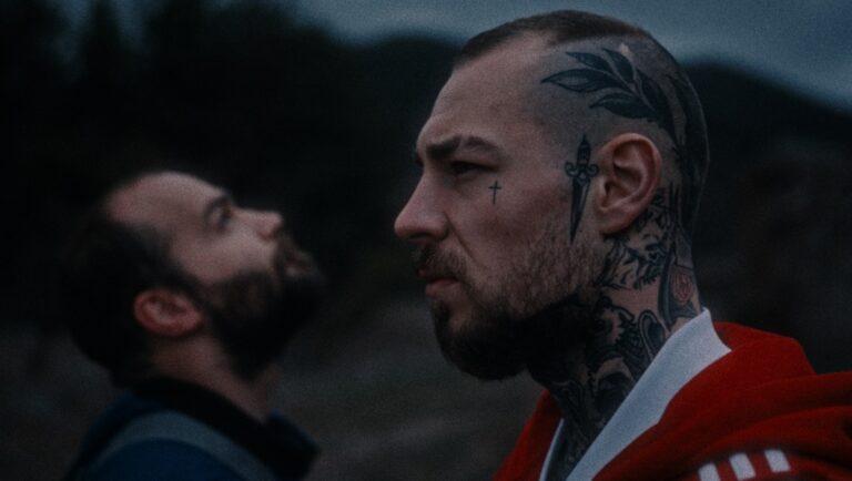 Tattooed man in profile. Man with beard looking up. Dark, moody. Tattoos on head, face, and neck.