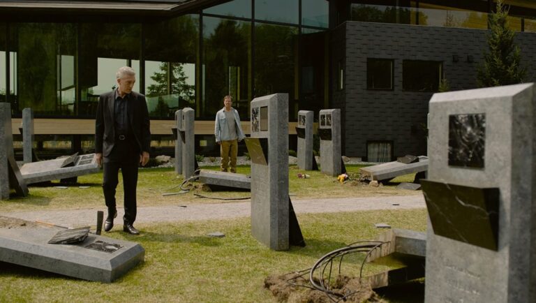 Still from The Shrouds, a David Cronenberg film. A man walks through a graveyard with modern headstones.