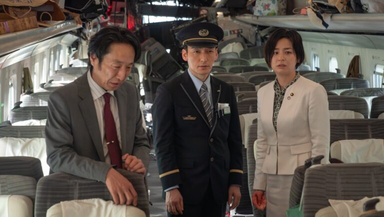 Bullet Train film scene: Asian man in suit, train conductor, & woman in white suit amidst train wreckage.