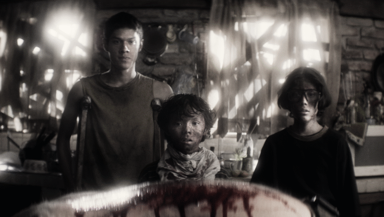 Black and white still from Parvulos. Three children stand behind a bloody surface. Horror film.