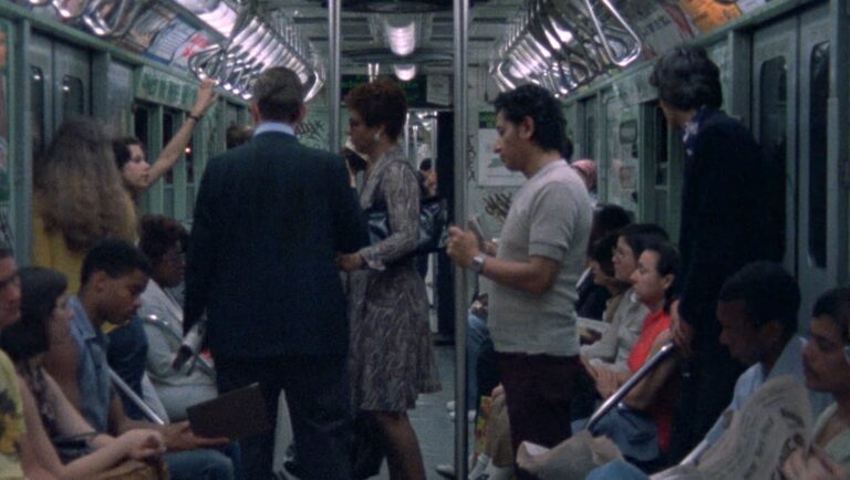 New York City subway scene. People ride the train, some standing and some seated. Commuters in transit.